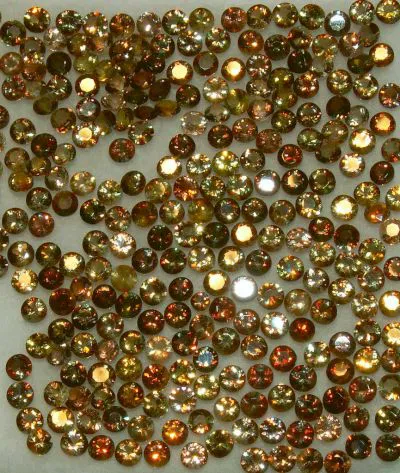 A scatter of faceted andalusite. If you look closely at these gems, you can see that many of them appear to be composed of a mosaic of color